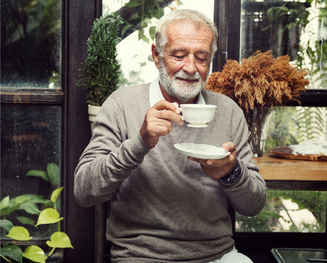 Older gentleman enjoying a hot drink surrounded by greenery. 