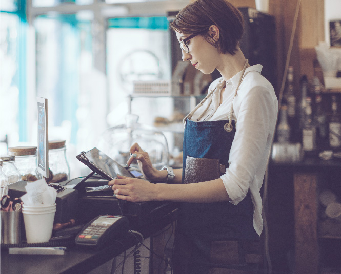 A young woman using a point of sale system in a coffee shop.